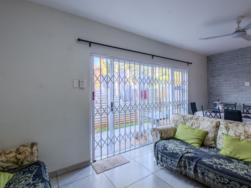 Living area featuring tiled floors, a ceiling fan, and an exposed brick wall, with direct access to the rear patio through a sliding glass door.