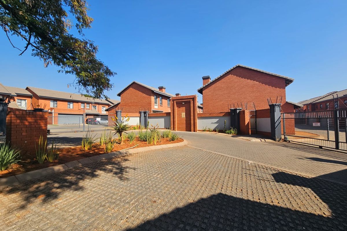 Front view of a townhouse complex featuring face brick architecture, paved driveway, and secure gated entrance with perimeter electric fencing.