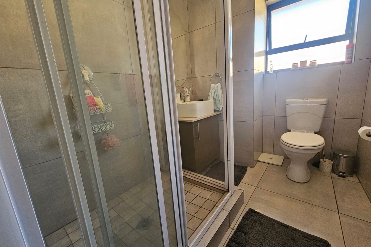A functional bathroom featuring a glass shower enclosure, a modern vessel sink with vanity cabinet, and a standard toilet with neutral floor-to-ceiling tiling.