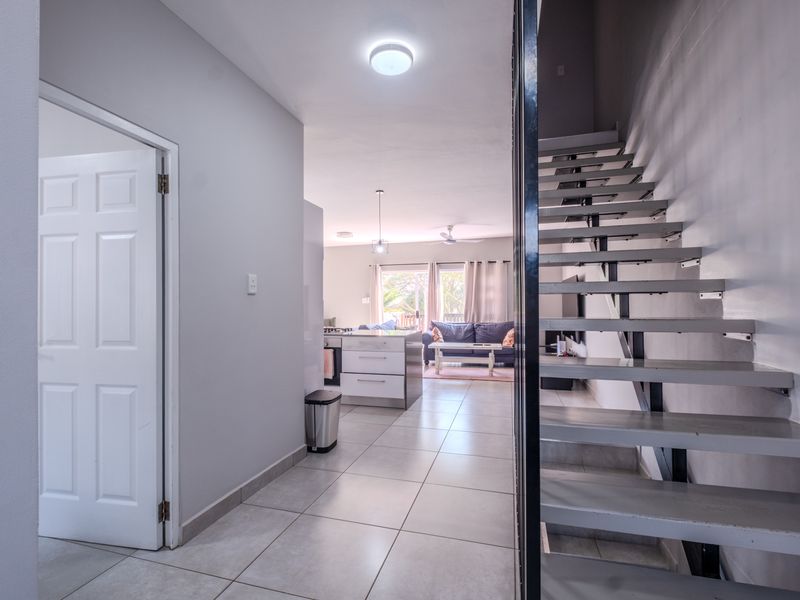 Open plan living area featuring a modern staircase, tiled flooring, and a central kitchen island, leading into a bright living space.