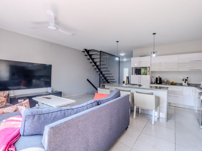 Modern open-plan living area featuring a contemporary kitchen with stone countertops, integrated appliances, and a striking staircase with metal balustrades.