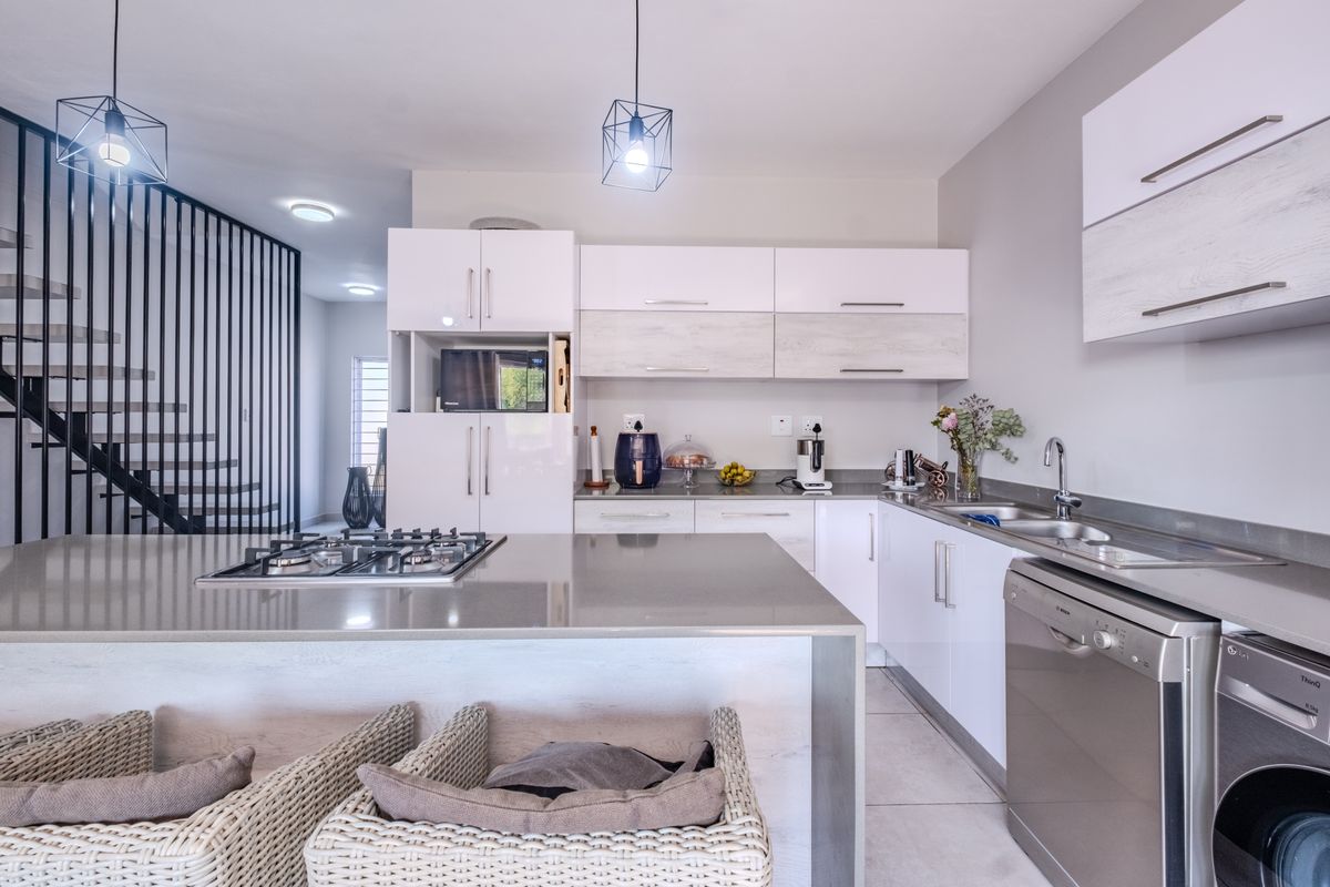 Modern kitchen featuring sleek white cabinetry, stone countertops, a gas hob, and integrated appliances, adjacent to an open-plan staircase with a contemporary metal balustrade.