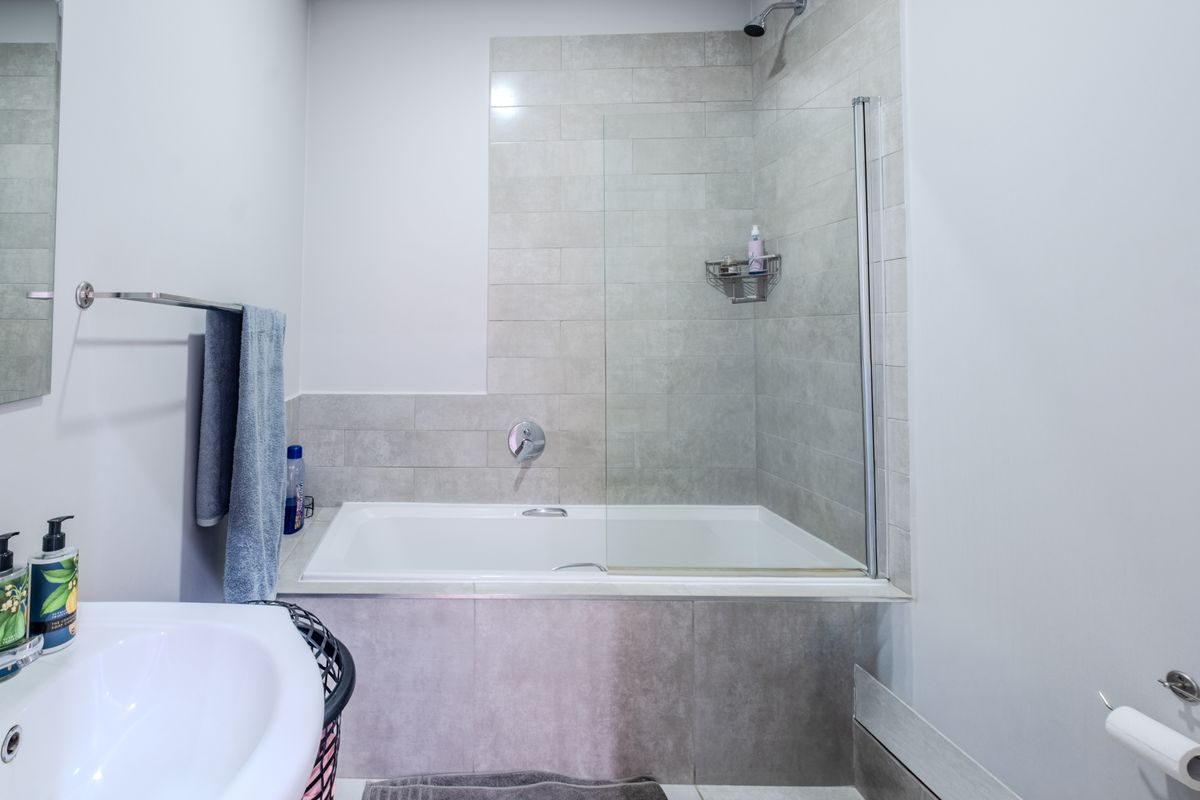 A modern bathroom featuring a built-in bathtub with a glass shower screen and neutral-toned wall tiling.