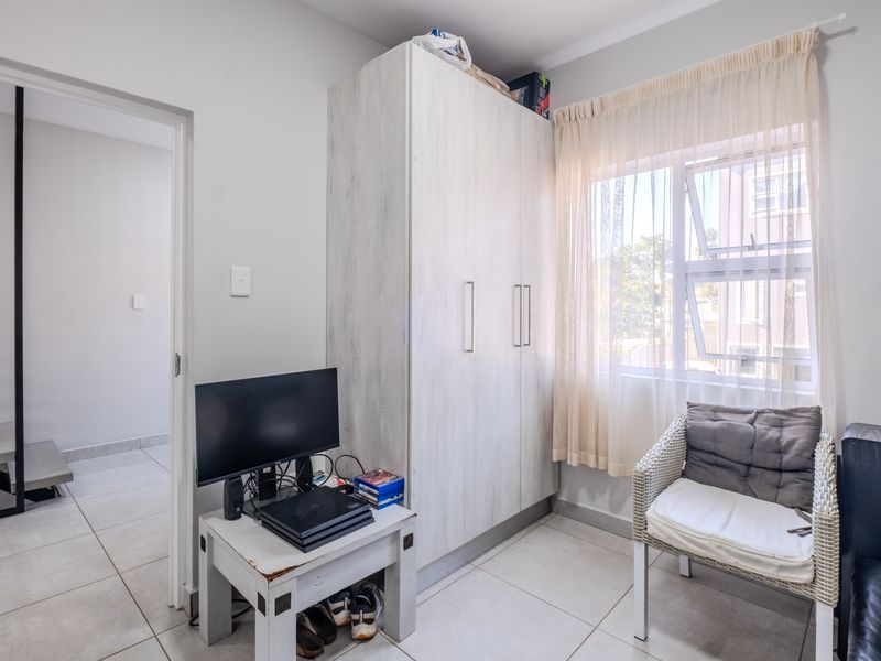 A bedroom featuring neutral tiled flooring, a built-in wardrobe, and natural light through an aluminium-framed window.