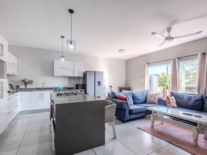 Modern open-plan living area featuring a sleek kitchen with a central island, gas hob, and direct access to an outdoor patio through sliding doors.