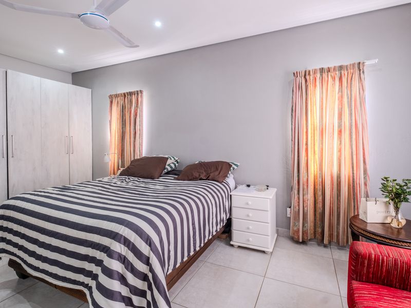 A well-lit bedroom featuring neutral grey walls, tiled flooring, a built-in wardrobe, and a ceiling fan.