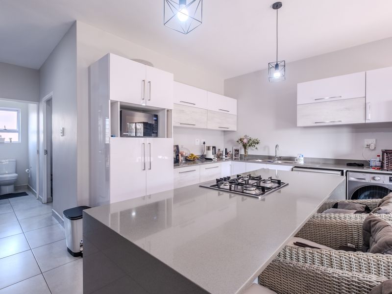 Modern open-plan kitchen featuring a central island with a gas hob, sleek white cabinetry, and high-quality finishes, seamlessly connected to the adjacent living area.