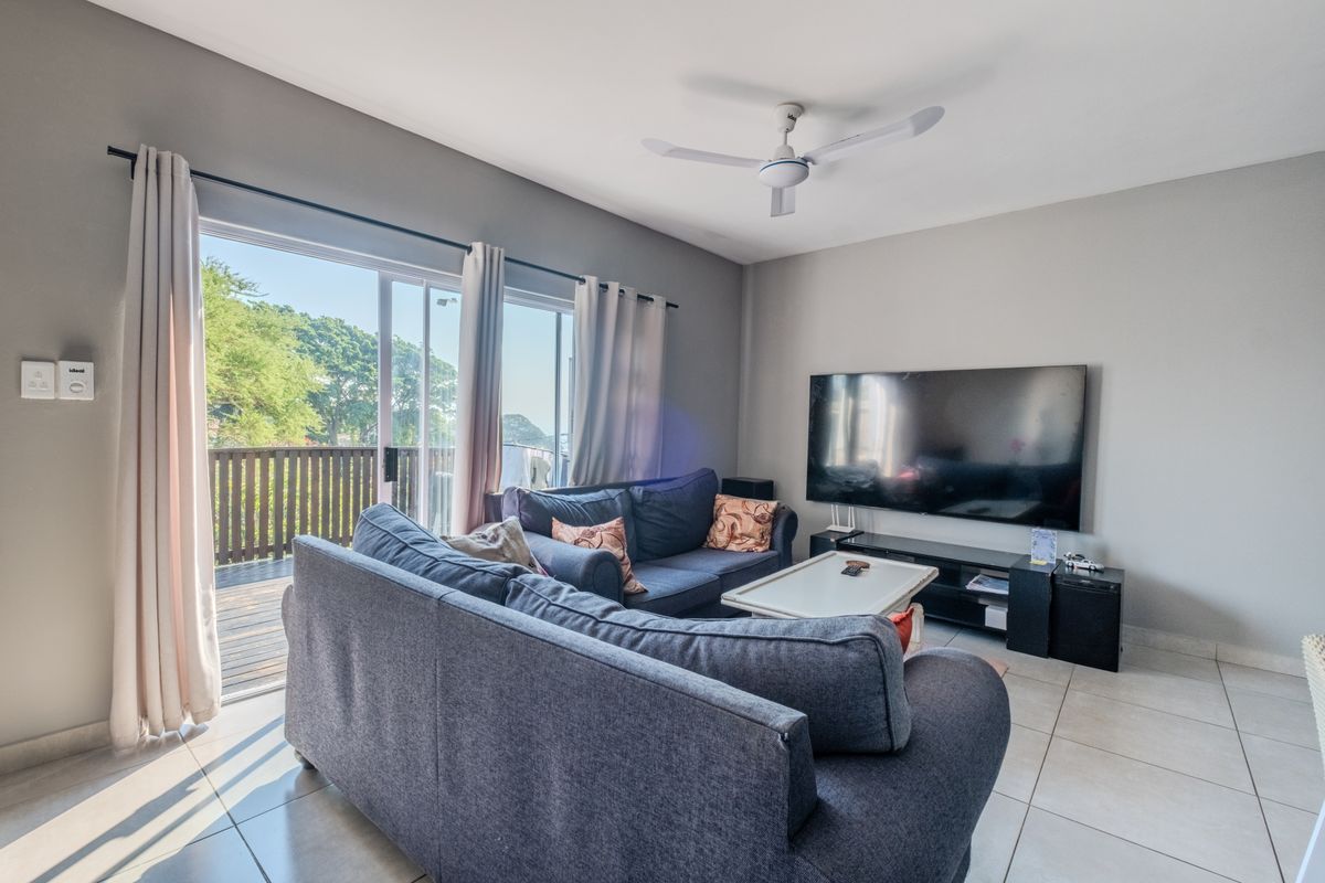A bright living room featuring tiled flooring, a ceiling fan, and large sliding glass doors that provide access to an outdoor balcony area.