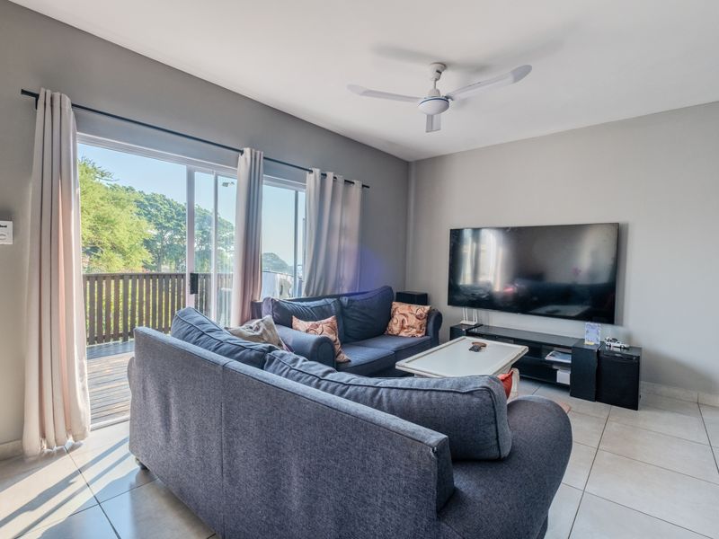 A bright living room featuring tiled flooring, a ceiling fan, and large sliding glass doors that provide access to an outdoor balcony area.