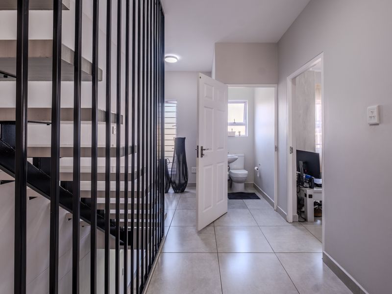 A bright, modern hallway featuring tiled flooring and a contemporary metal staircase balustrade, providing access to adjacent rooms.
