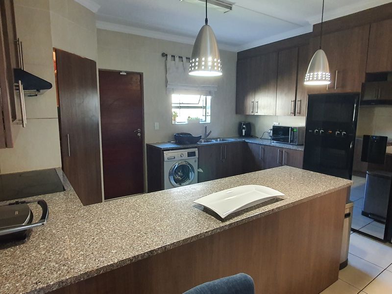 A functional kitchen featuring dark wood cabinetry, granite countertops, integrated appliances, and an adjoining scullery area with tiled flooring.