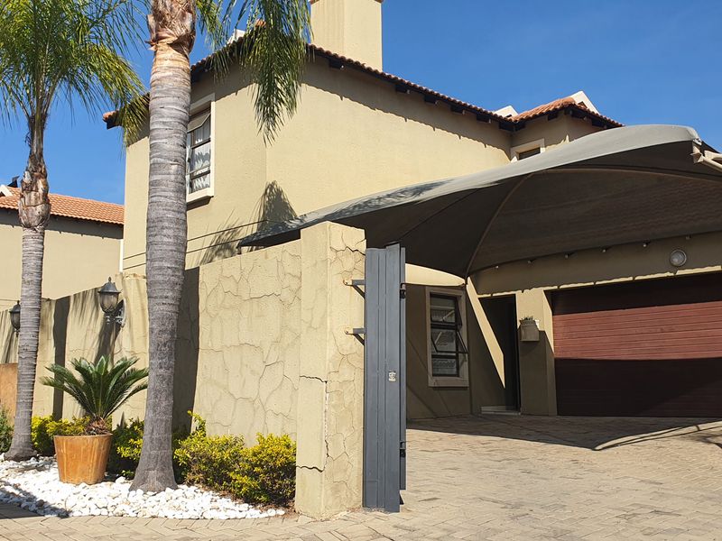 Front elevation of a cluster home featuring a paved driveway, shade sail carport, and a sectional garage door.