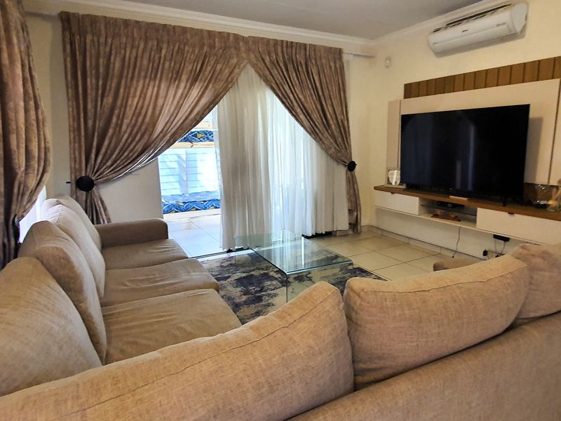 A comfortable living room featuring tiled flooring, a built-in media console, and a sliding glass door providing access to the patio area.