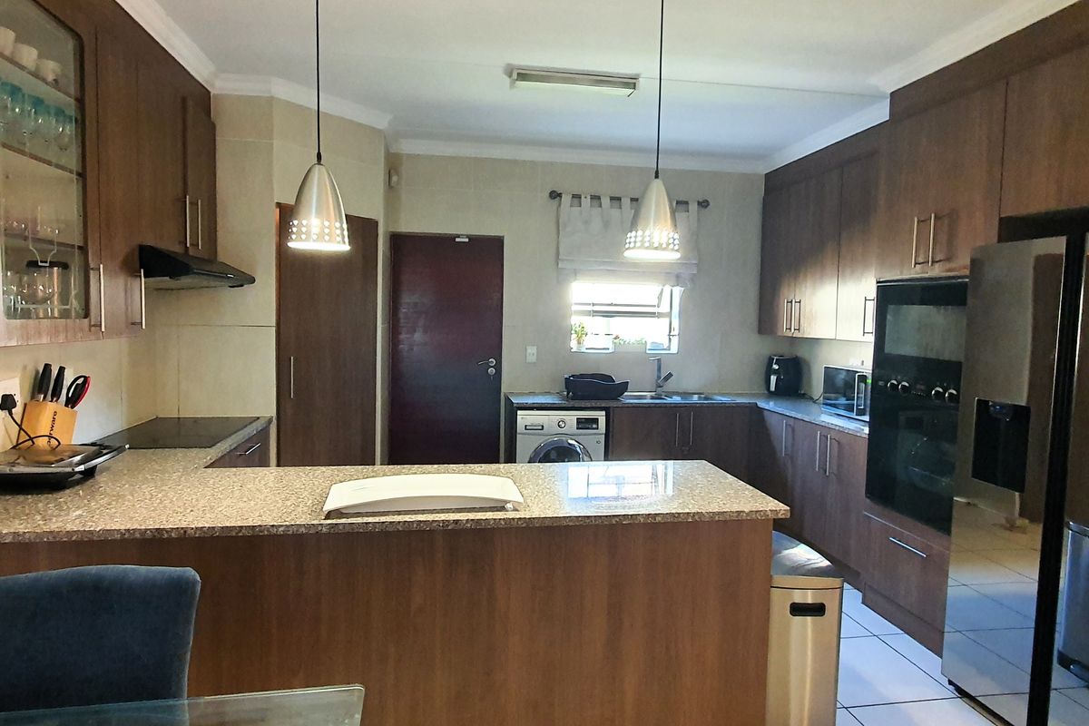 A functional kitchen featuring dark wood cabinetry, granite countertops, built-in oven, hob, and an integrated laundry area with a sink.