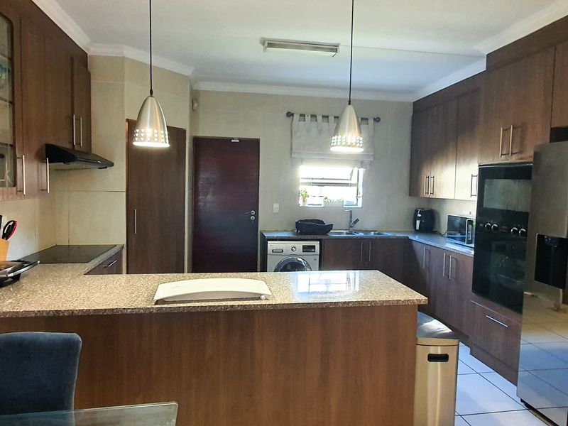 A functional kitchen featuring dark wood cabinetry, granite countertops, built-in oven, hob, and an integrated laundry area with a sink.
