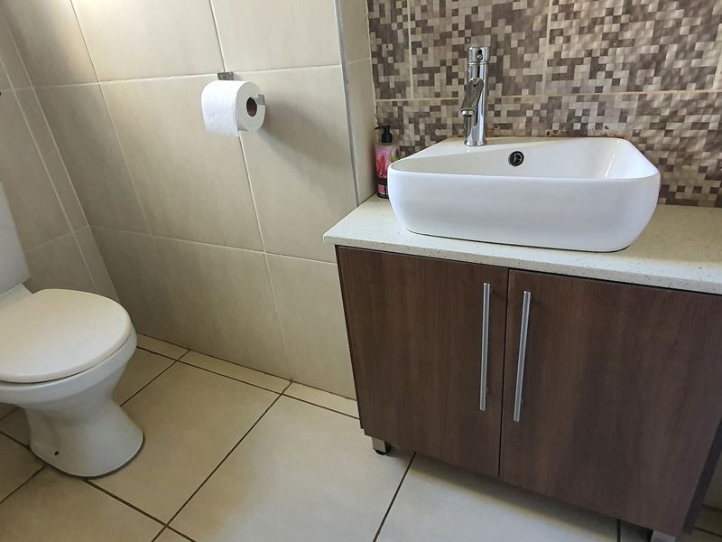A compact bathroom featuring a modern vessel basin on a vanity cabinet, tiled flooring, and a decorative mosaic tiled feature wall.