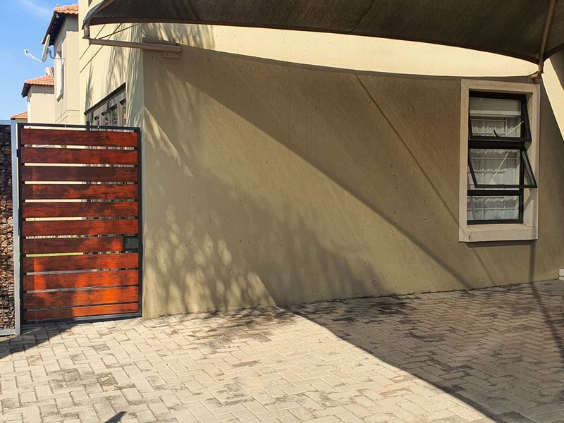 Front exterior view of the cluster property featuring a paved driveway, shade sail, gabion wall, timber gate, and a sectional garage door.