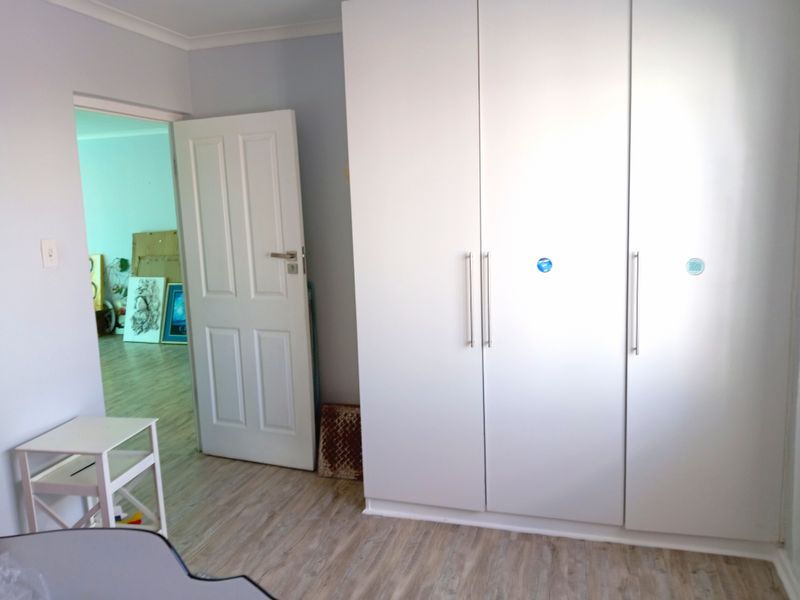 A clean, empty bedroom featuring modern white built-in cupboards and light-toned laminate flooring, offering a neutral canvas for personalization.