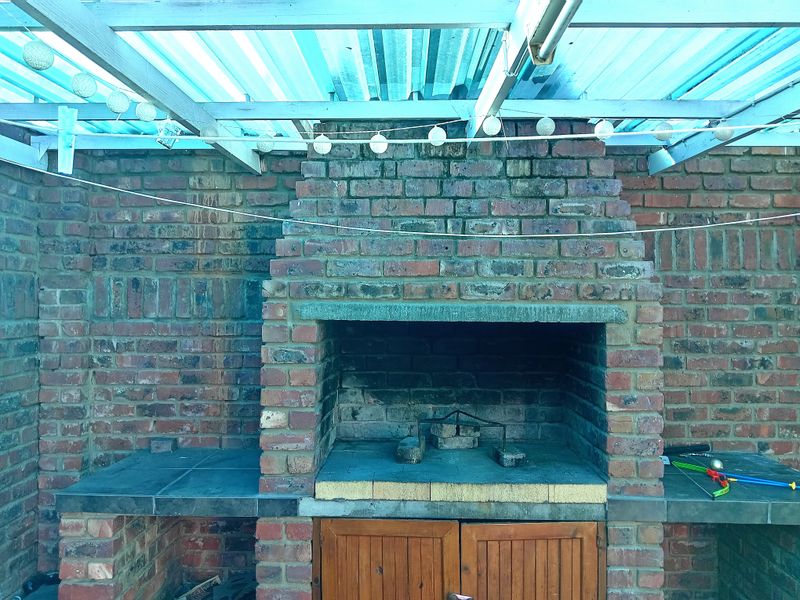Outdoor patio area featuring a traditional built-in brick braai with tiled prep surfaces and a covered roof structure.