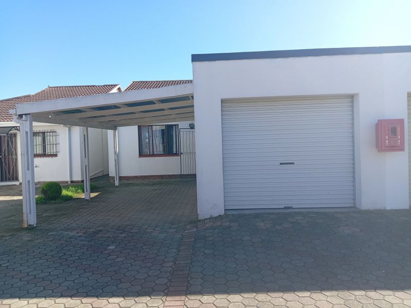 Exterior view of a townhouse featuring a single enclosed garage with a roller door and an adjacent covered carport area with paved driveway.