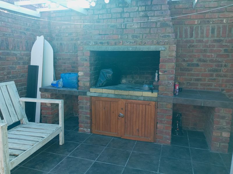 Outdoor patio area featuring a built-in brick braai with tiled preparation surfaces and wooden storage cabinetry, ideal for entertaining.
