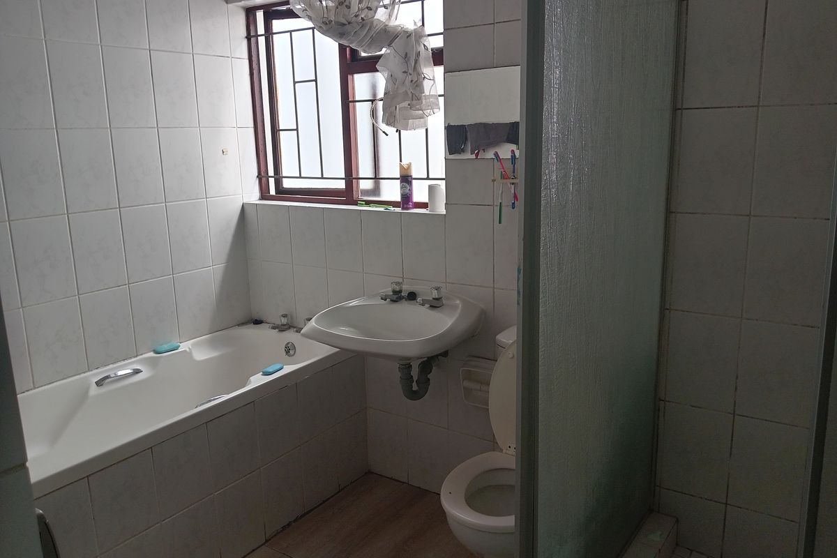 A functional bathroom featuring a bathtub, pedestal basin, toilet, and separate shower enclosure with tiled walls and security bars on the window.