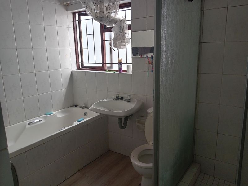 A functional bathroom featuring a bathtub, pedestal basin, toilet, and separate shower enclosure with tiled walls and security bars on the window.