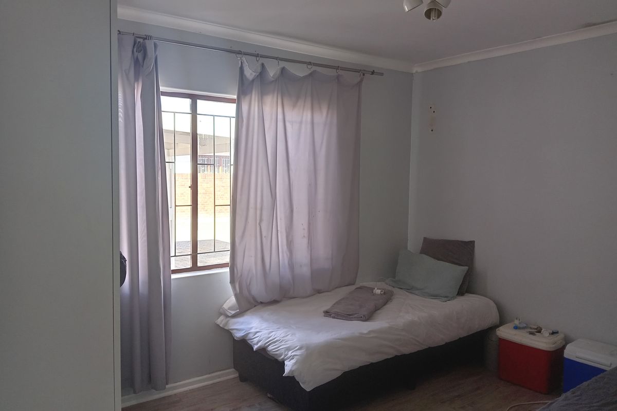 A standard bedroom featuring laminate flooring, a built-in wardrobe, and a window fitted with security bars.