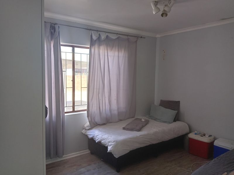 A standard bedroom featuring laminate flooring, a built-in wardrobe, and a window fitted with security bars.