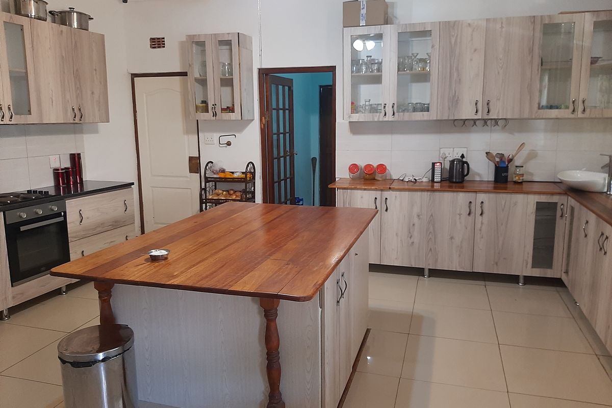 Spacious kitchen featuring light wood-grain cabinetry, a large central wooden island, built-in oven, and tiled flooring throughout.