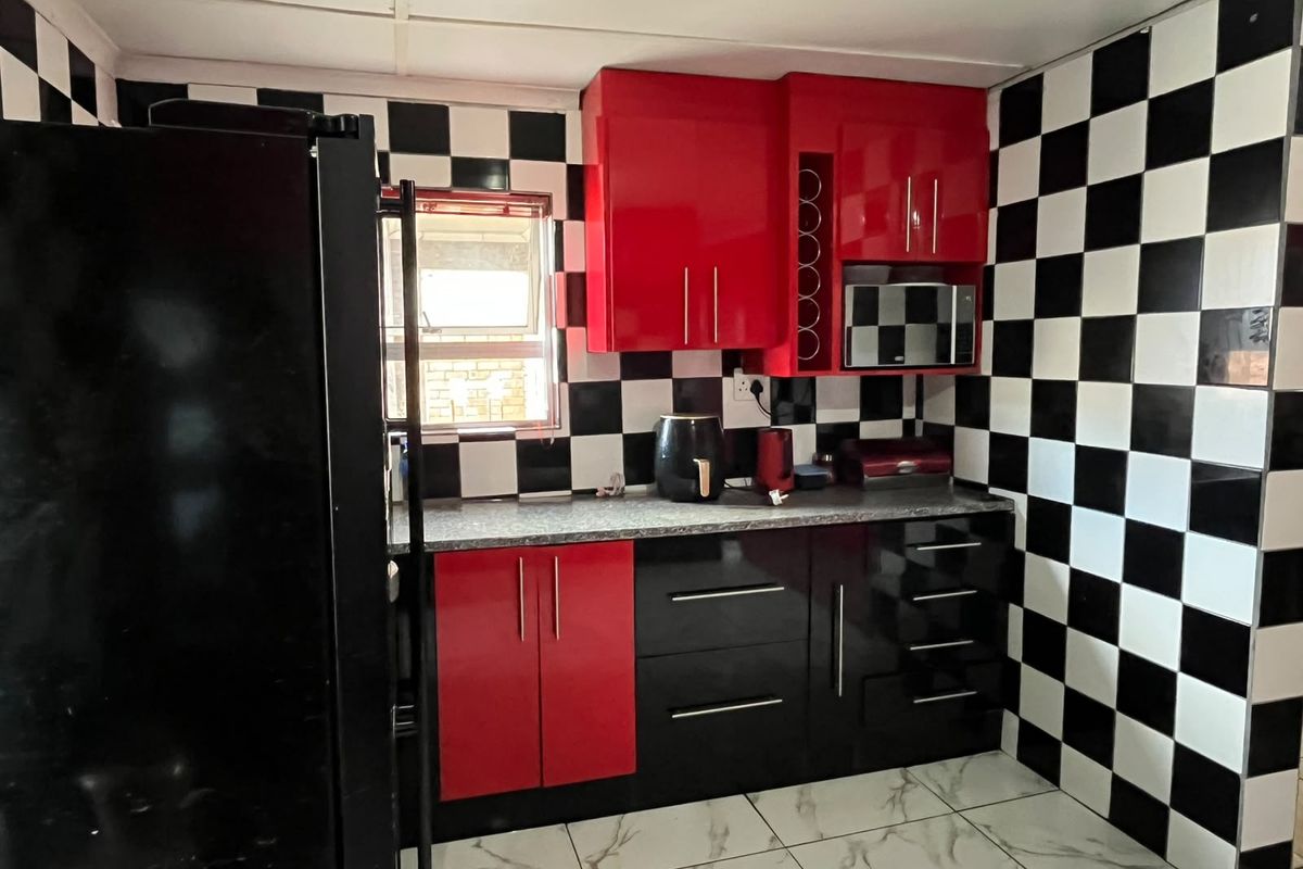 A compact kitchen featuring high-contrast red and black cabinetry, a checkerboard tiled splashback, and marble-effect floor tiles.