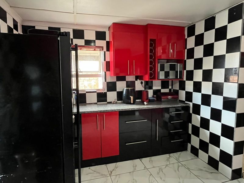 A compact kitchen featuring high-contrast red and black cabinetry, a checkerboard tiled splashback, and marble-effect floor tiles.