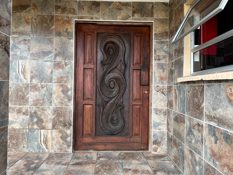 A well-maintained entrance featuring a decorative carved wooden front door set against natural stone tile wall cladding and matching floor tiles.