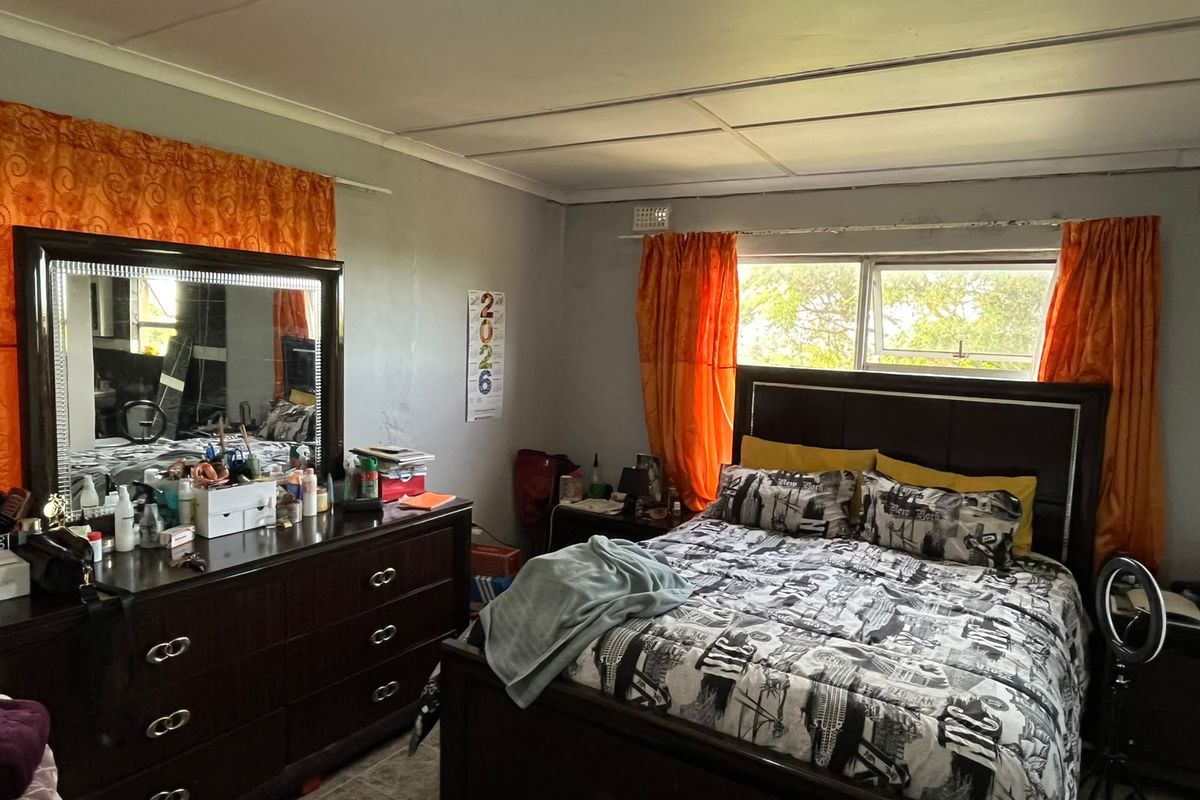 A bedroom featuring tiled flooring, a sliding window with visible wear on the frame, and panelled ceiling finishes.