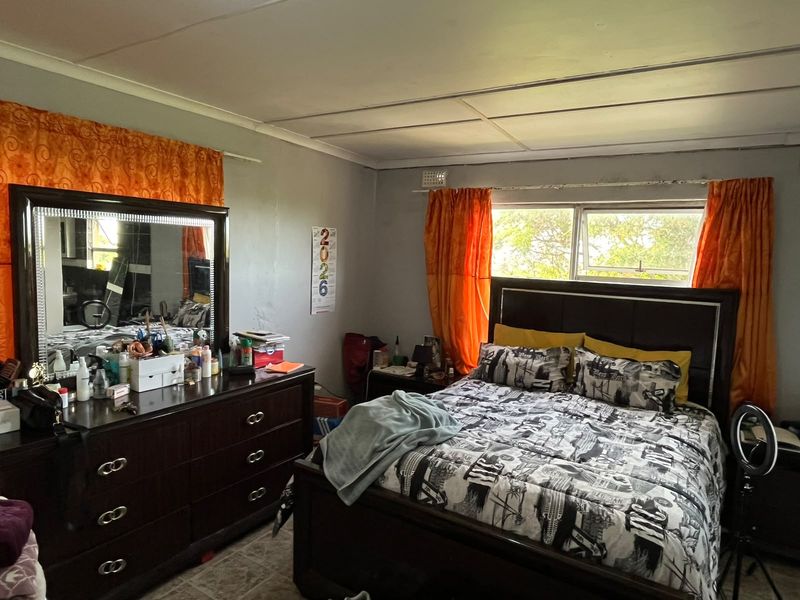 A bedroom featuring tiled flooring, a sliding window with visible wear on the frame, and panelled ceiling finishes.