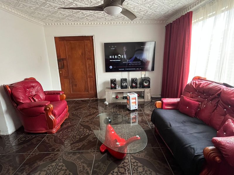 A living room featuring decorative ceiling tiles, a ceiling fan, and dark patterned floor tiles.