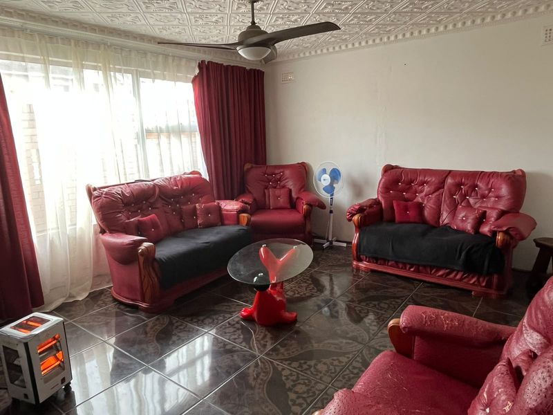 A living room featuring decorative ceiling tiles, a ceiling fan, and dark tiled flooring, providing a functional space with natural light from a large window.