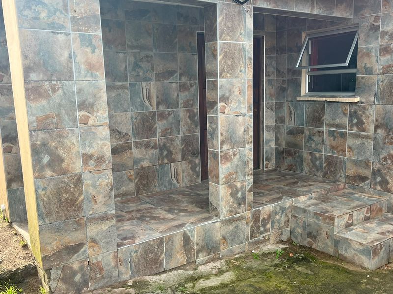 A covered patio area featuring full slate tile cladding on walls and floors, with integrated steps and a top-hung window.