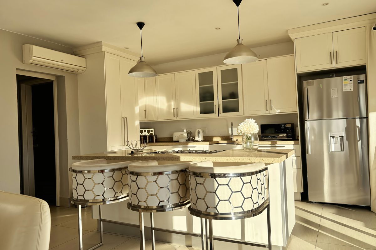 Modern kitchen featuring a central island with stone countertops, gas hob, ample cabinetry, and integrated appliances, finished with tiled flooring and pendant lighting.