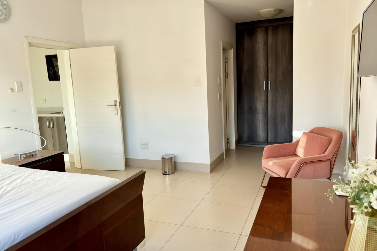 Spacious bedroom featuring neutral tiled flooring, built-in dark wood cabinetry, and direct access to an adjoining room.