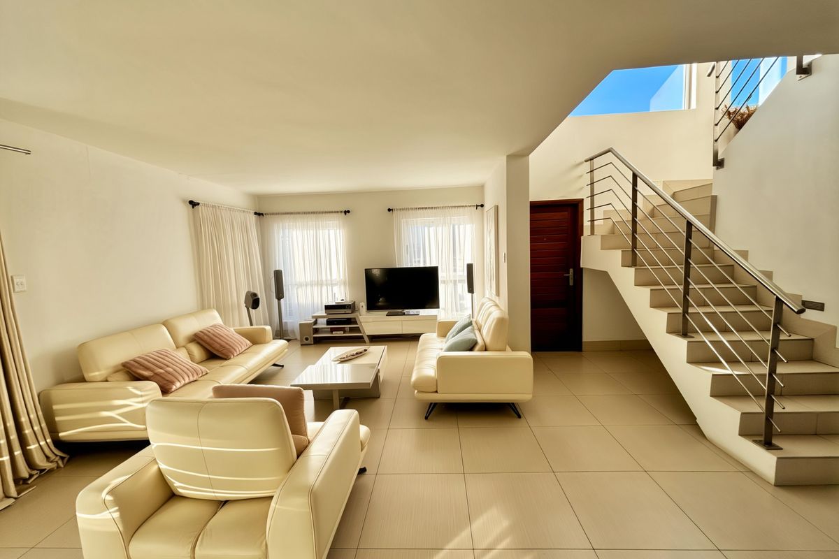 Spacious open-plan living area featuring large format floor tiles, a modern staircase with stainless steel railings, and abundant natural light.