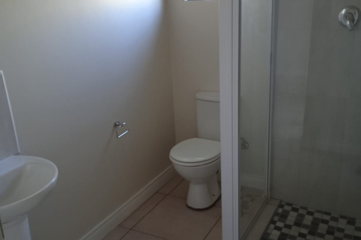 A functional bathroom featuring a pedestal basin, a standard toilet, and a shower enclosure with tiled flooring and security bars on the window.