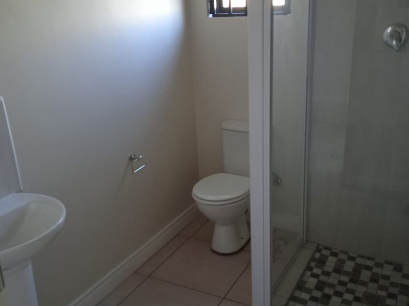 A functional bathroom featuring a pedestal basin, a standard toilet, and a shower enclosure with tiled flooring and security bars on the window.