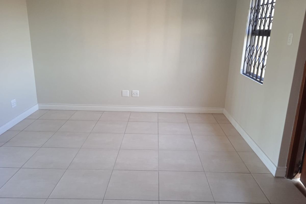 A clean, empty bedroom featuring neutral tiled flooring, light-colored walls, and a window fitted with a security gate.