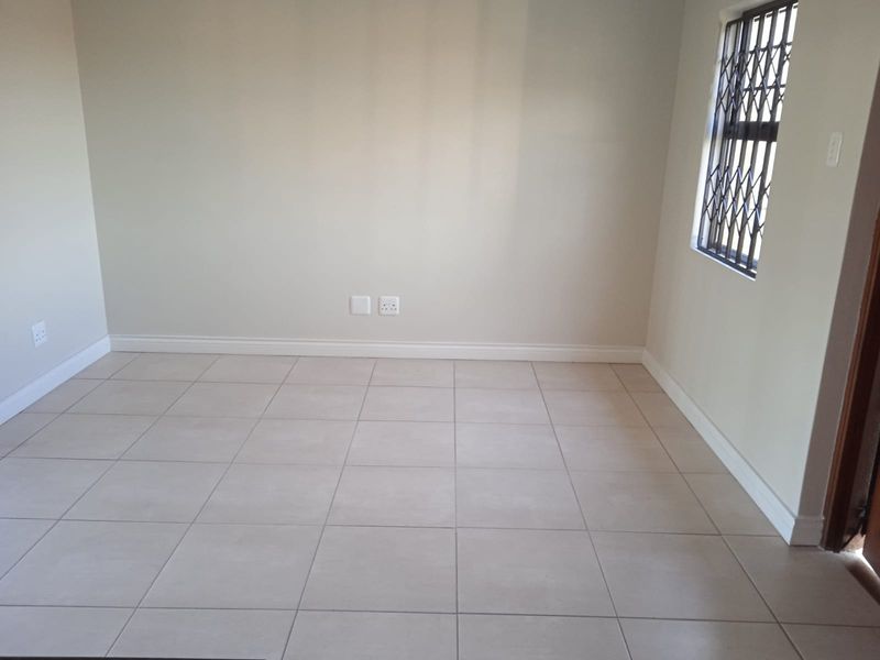 A clean, empty bedroom featuring neutral tiled flooring, light-colored walls, and a window fitted with a security gate.