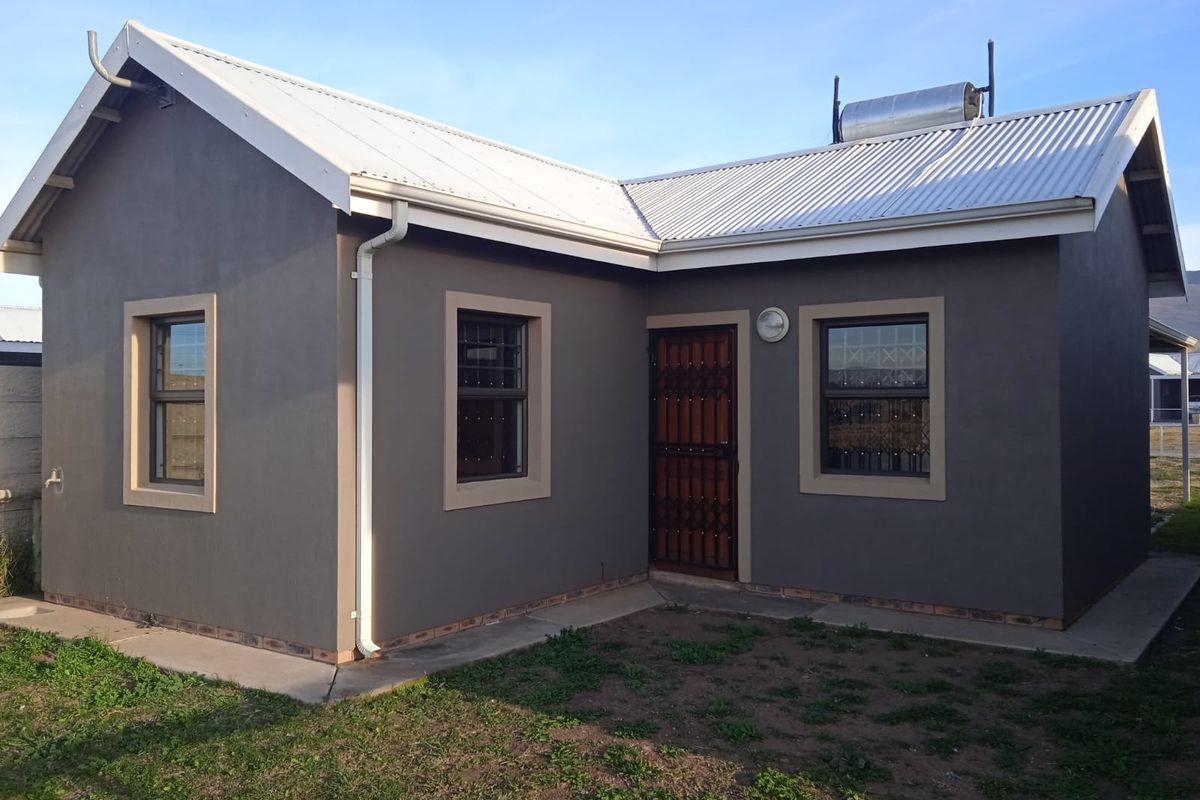 Rear view of a modern house featuring a grey rendered facade, corrugated metal roof, solar water heater, and secure window bars.