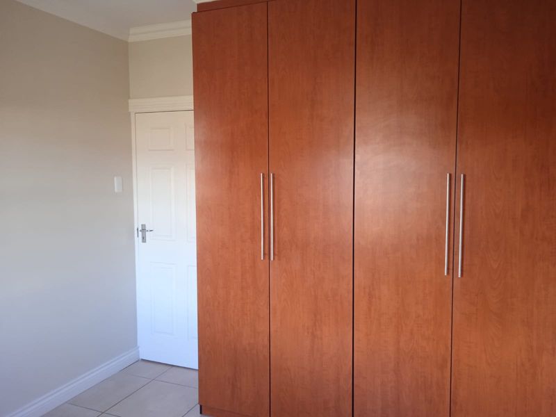 A clean bedroom interior featuring built-in wooden cupboards, neutral wall finishes, and tiled flooring.
