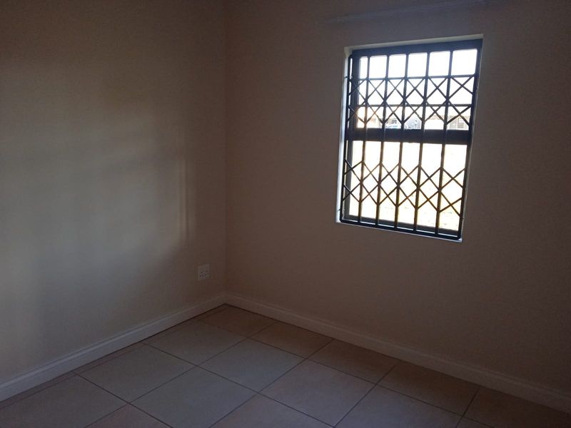 A clean, empty bedroom featuring neutral tiled flooring and a window fitted with a security gate.