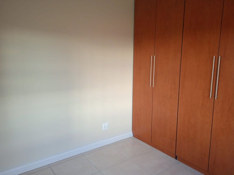 A clean, empty bedroom featuring neutral walls, tiled flooring, and modern wood-finish built-in cupboards with sleek metal handles.