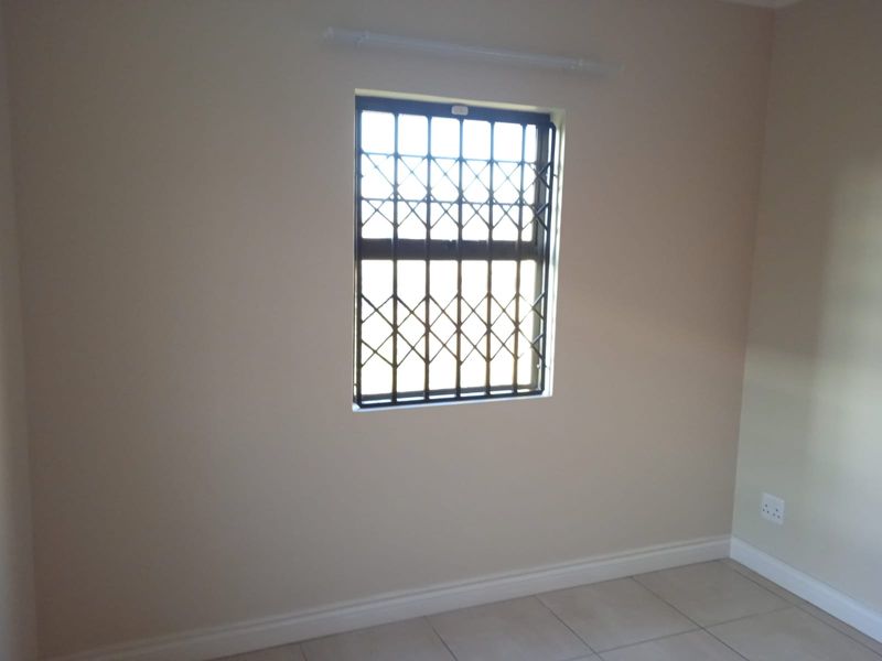 A clean, empty bedroom featuring neutral wall paint, tiled flooring, and a window fitted with a security gate.